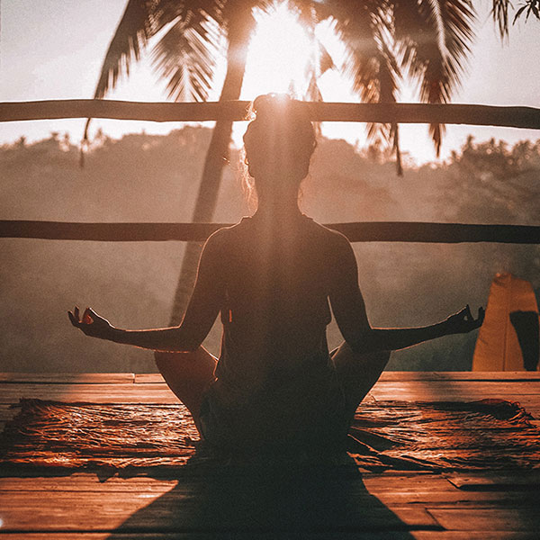 Žena sedící proti slunci v meditační poloze.
